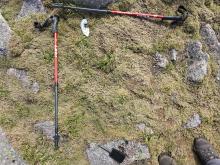 Sample location C with hiking poles displaying reference grid. Rocky terrain with thin layer of soil underneath thick dry moss.