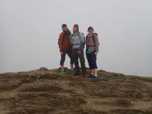 Three women in hiking gear at the informal top of Being Ghlas with white cloud obscuring the view behind them